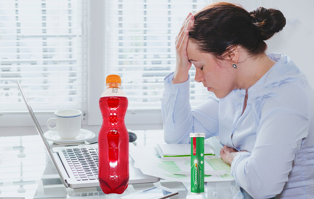 Hungover woman at desk with berocca