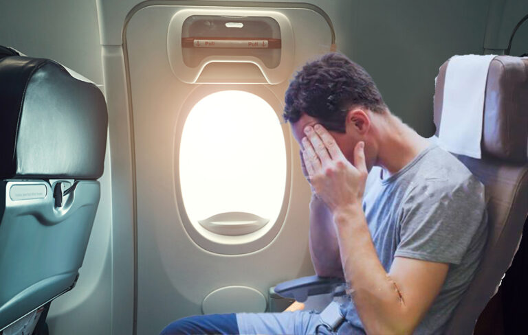 Man sitting in aeroplane emergency exit row with head in his hands