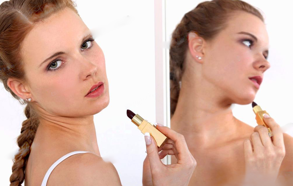 woman reluctantly applying lipstick while looking in the mirro