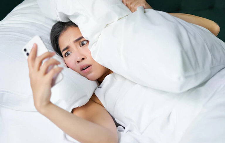 Panicked woman in bed looking at her phone.