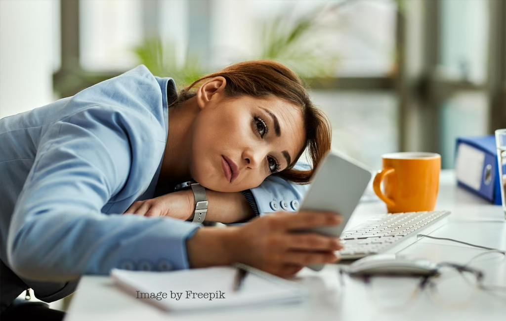 woman slumped on desk looking at phone