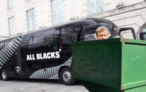 Razor Robertson in skip bin with all blacks bus and hotel in background.