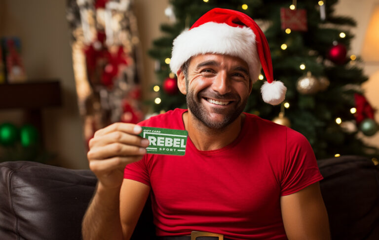 35 year old man wearing santa hat smiling with rebel sport voucher in hand