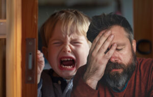 man facepalms while child cries